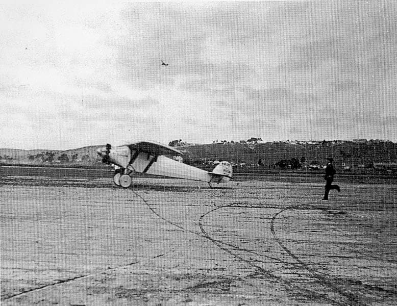 Airfield photograph of the Spirit of St. Louis landing rollout at Dutch Flats with a man running across the dirt field.