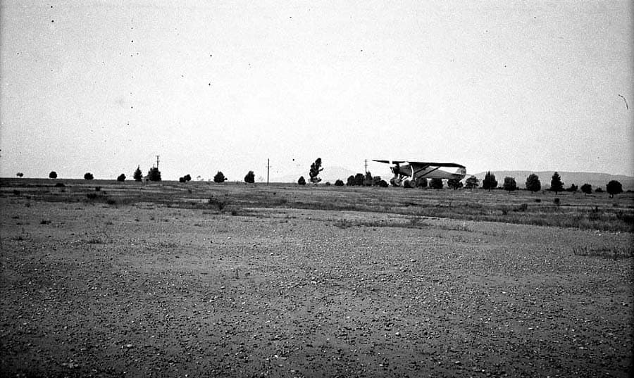 Long-distance airfield photograph of the Spirit of St. Louis airborne low over the Camp Kearny flight field.