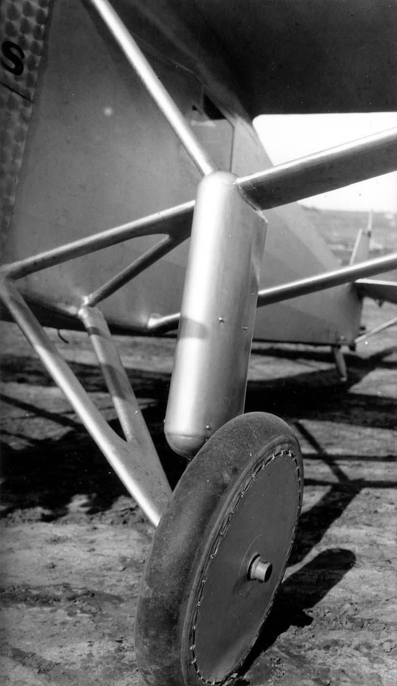 Low ground-level view of the right split-axle landing gear, shock strut fairing, and covered wire wheel.