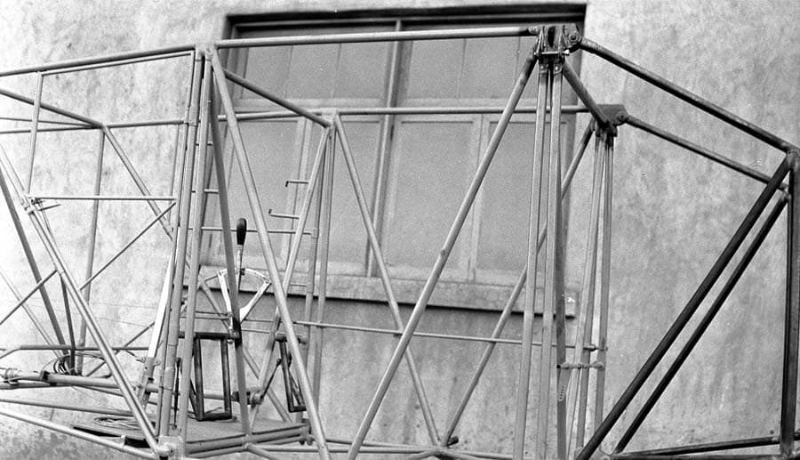 Close-up view of bare fuselage frame outside factory showing cockpit floor, control stick, and throttle lever mounts.