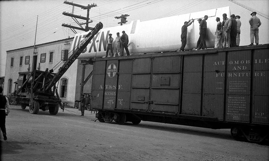 Workers standing on the roof of a Santa Fe boxcar guiding the suspended 46-foot wing of the Spirit of St. Louis.