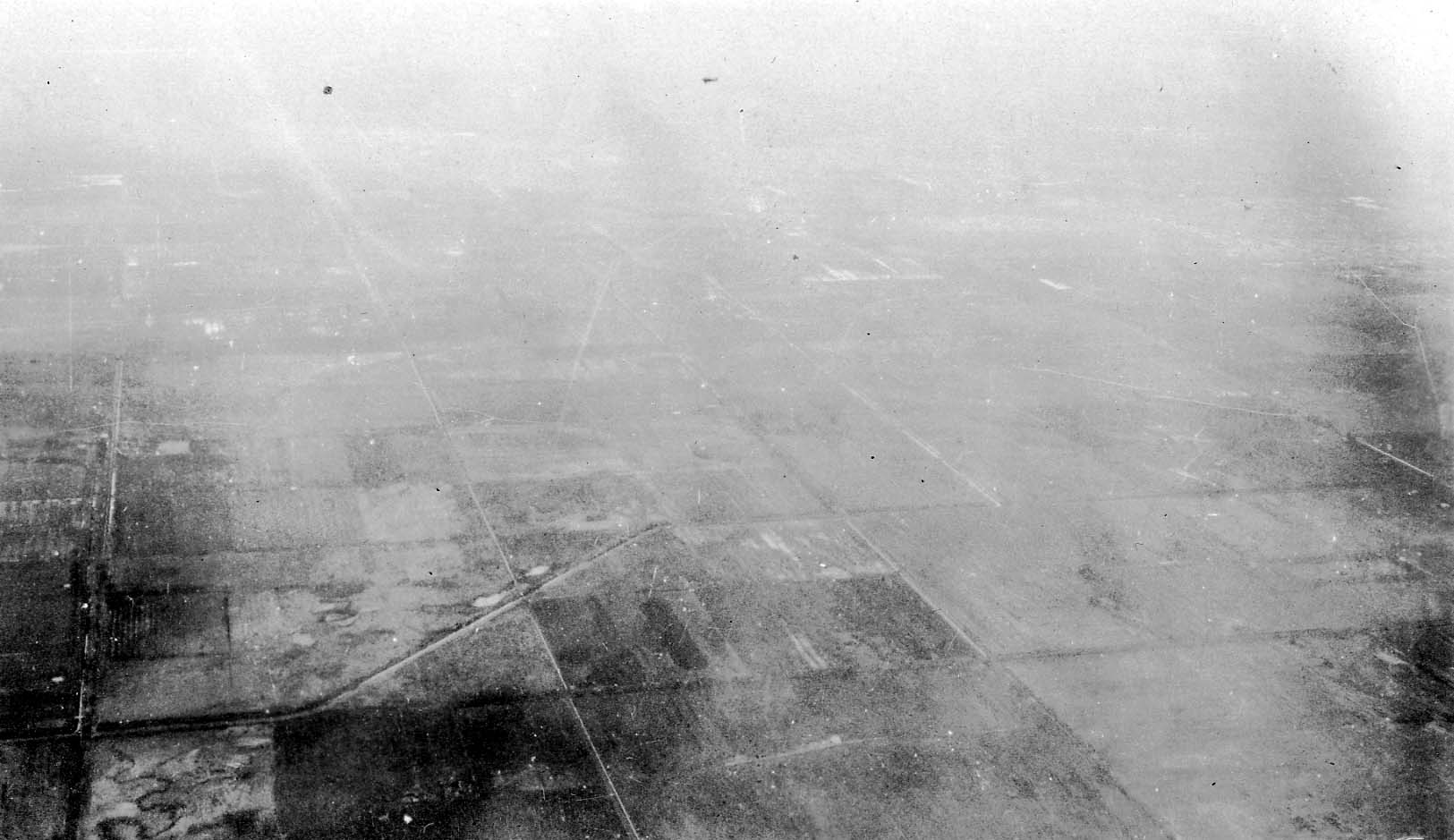 A high-altitude aerial view of expansive, flat agricultural fields divided by a grid of straight roads.
