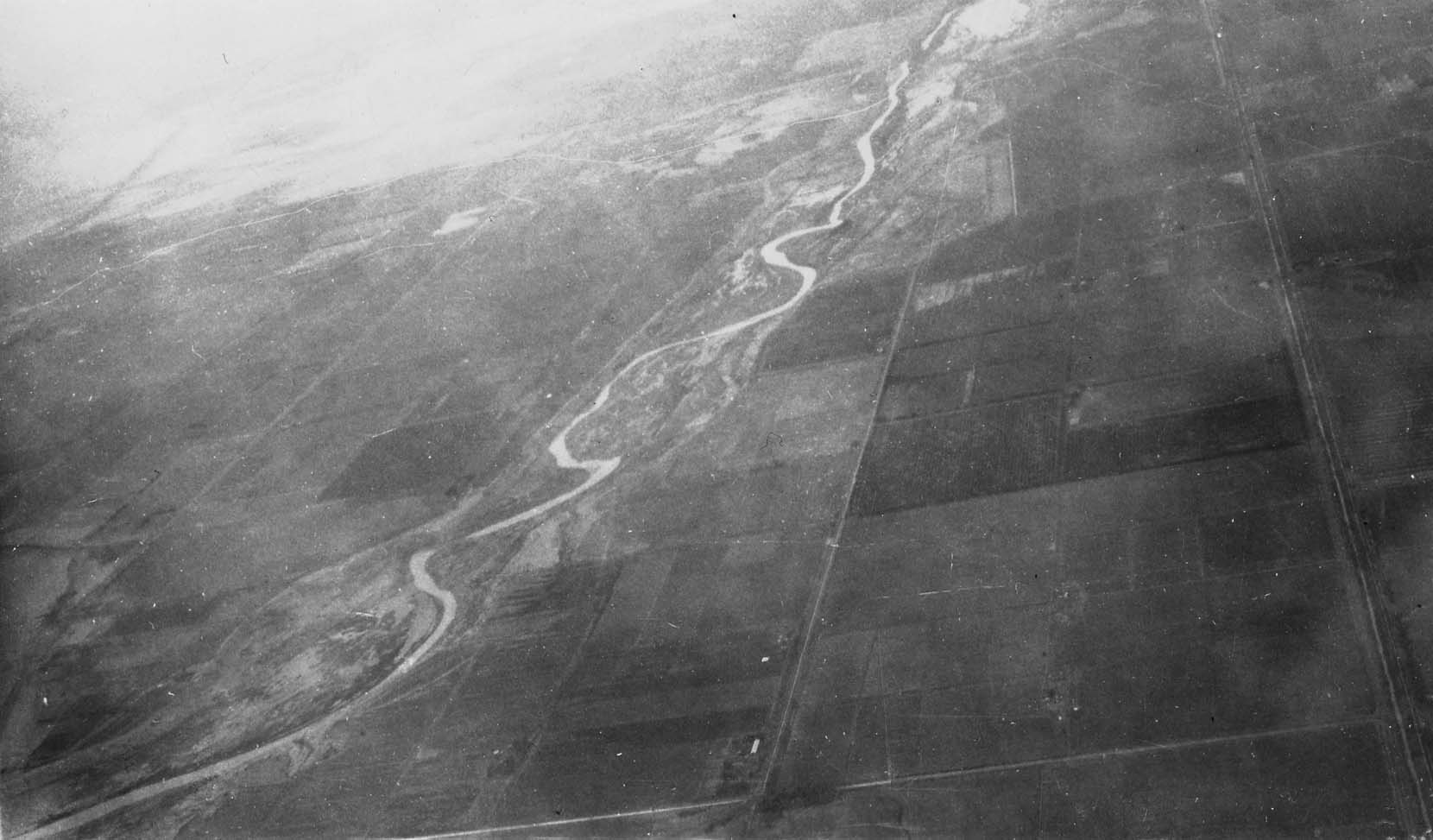 A high-altitude aerial photograph showing a river winding heavily through flat, sectioned agricultural land.