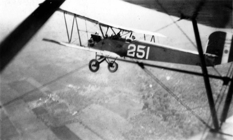 An air-to-air photograph of a Army trainer biplane bearing the number 251, flying over patterned fields below in Texas