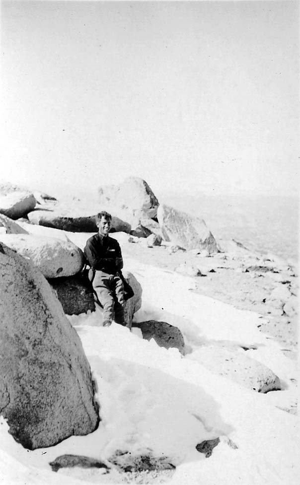 Donald A. Hall Sr. smiling while resting against granite boulders in a high-altitude mountain snowfield.