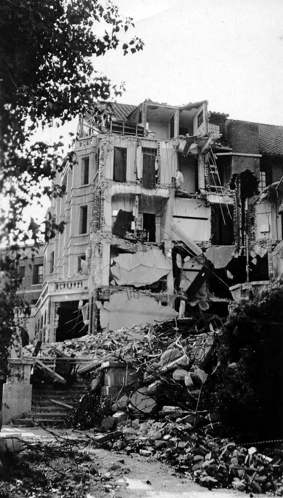 The sheared facade of the Spanish Revival Arlington Hotel showing guest rooms torn open to the elements and piles of structural rubble.