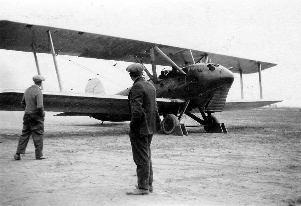 A front three-quarter view of an experimental military pursuit biplane with a large pointed nose spinner, tunnel radiator, and heavy wheel chocks.