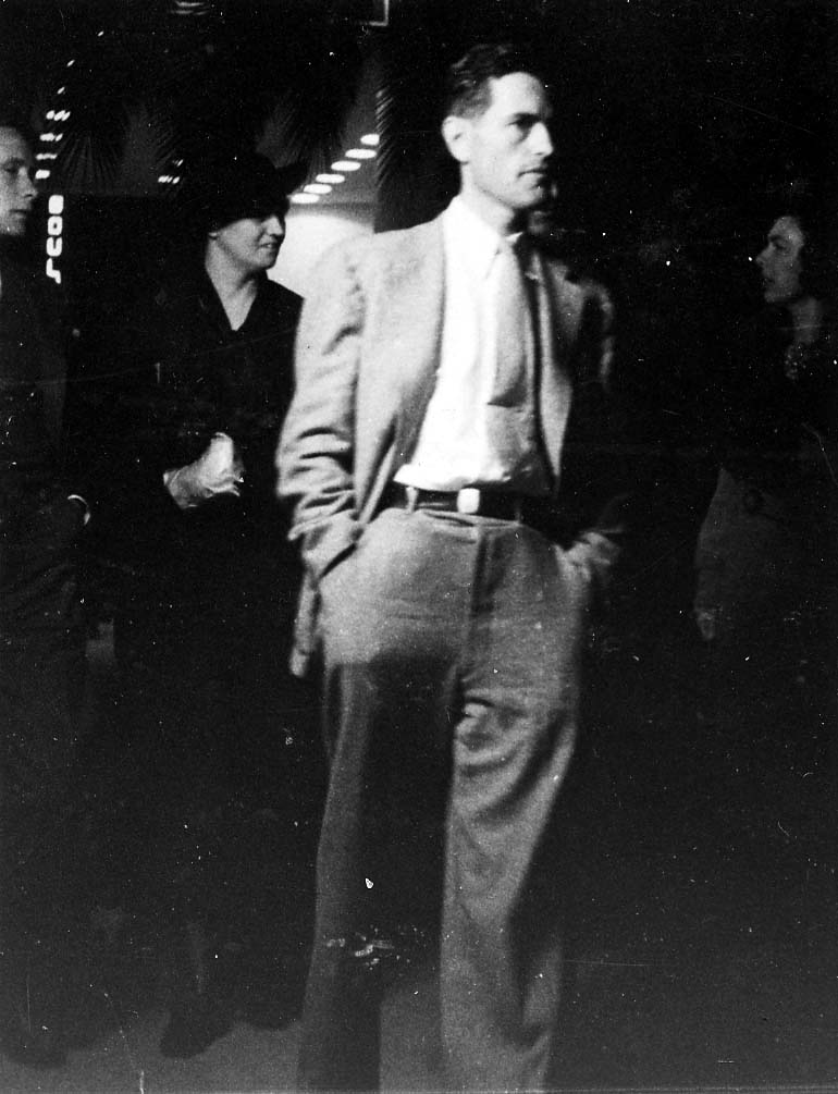 Candid photograph of Donald A. Hall Sr. in a light suit and tie walking through an indoor gathering.