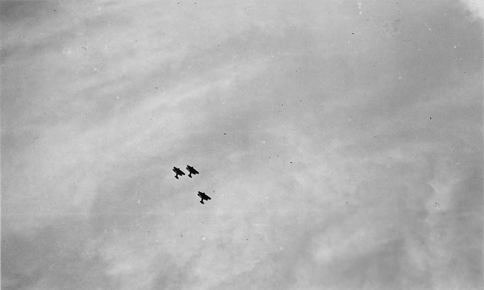 Three vintage biplanes flying in a tight V-formation high against a hazy, cloudy sky.