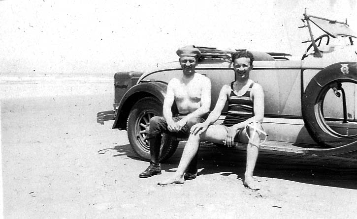 Two smiling young men sitting on the running board of Donald A. Hall Sr.'s 1925 Studebaker Roadster parked on a wide sandy beach.