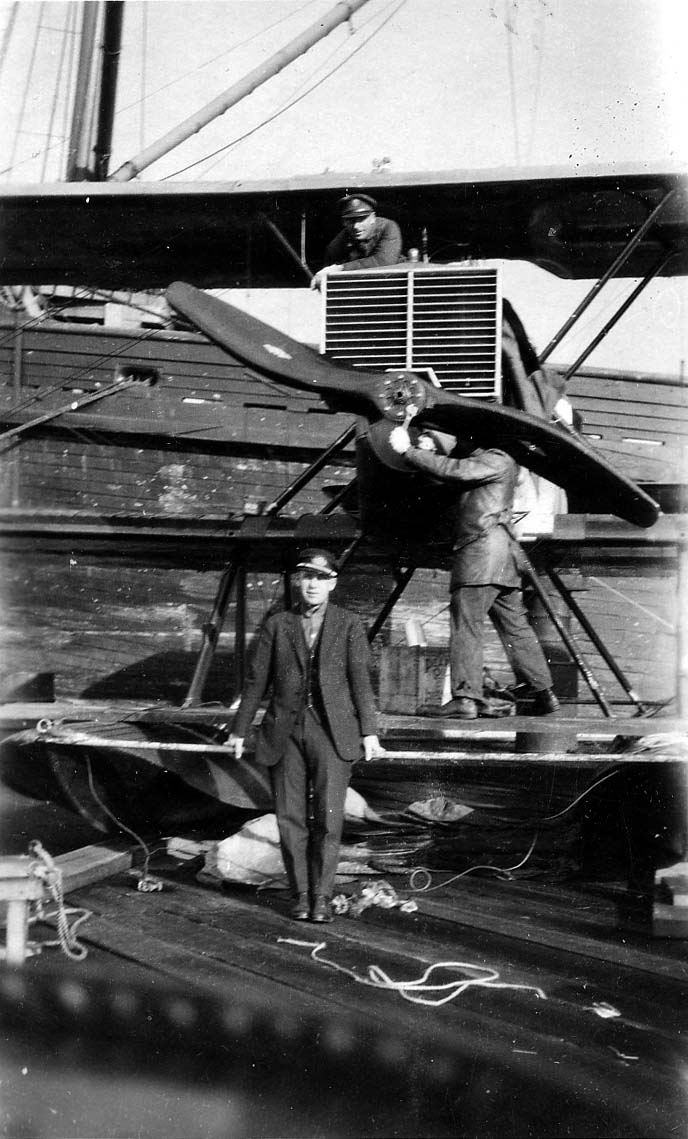 Mechanics adjusting the wooden propeller of a Douglas World Cruiser seaplane with an officer standing on the pontoon in the foreground.