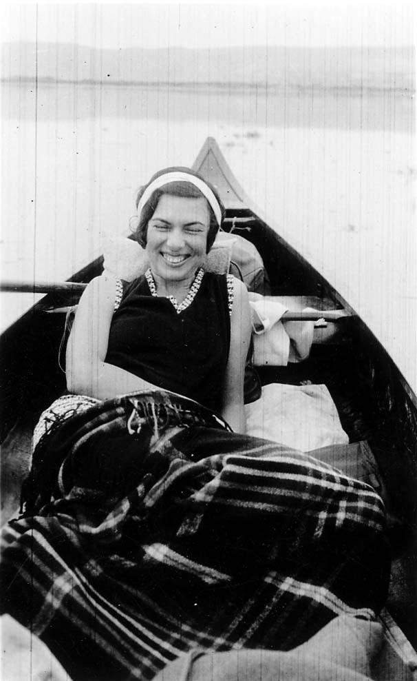 A close-up portrait of Elisabeth "Betty" Hall laughing brightly while reclining comfortably in a canoe, wrapped in a plaid blanket.