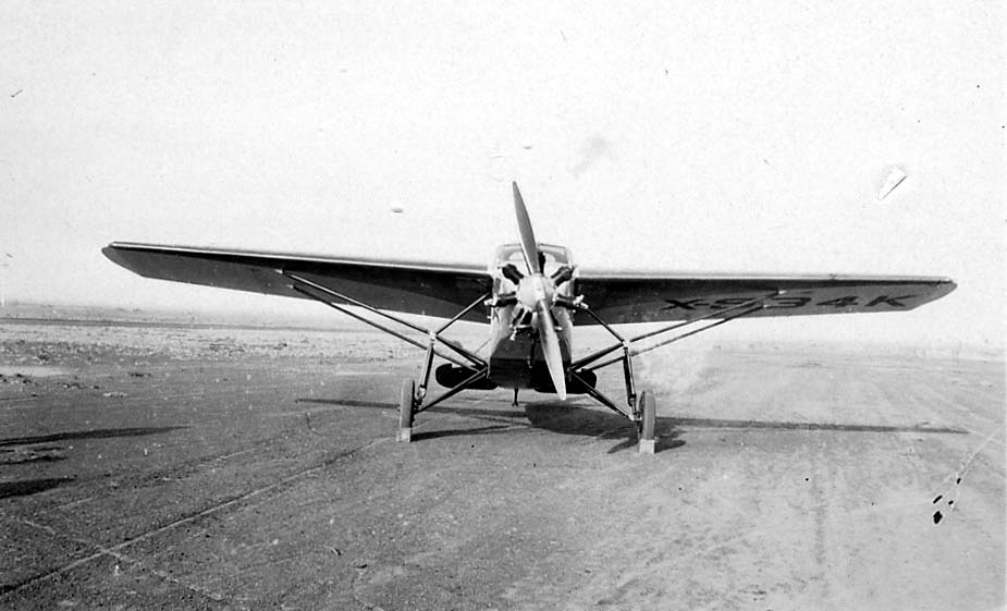 Frontal view of an experimental high-wing cabin monoplane with an uncowled radial engine on a paved runway with wing markings.