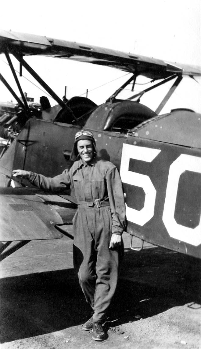 A smiling flight cadet in a parachute harness leaning against the fuselage of a training biplane marked with a large number 50.