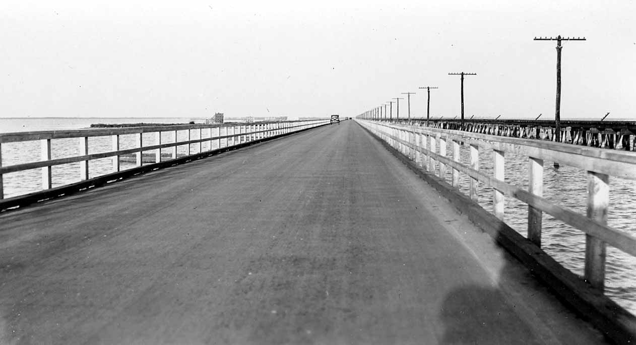 A long, straight wooden bridge stretching far into the distance over a body of water, flanked by utility poles.