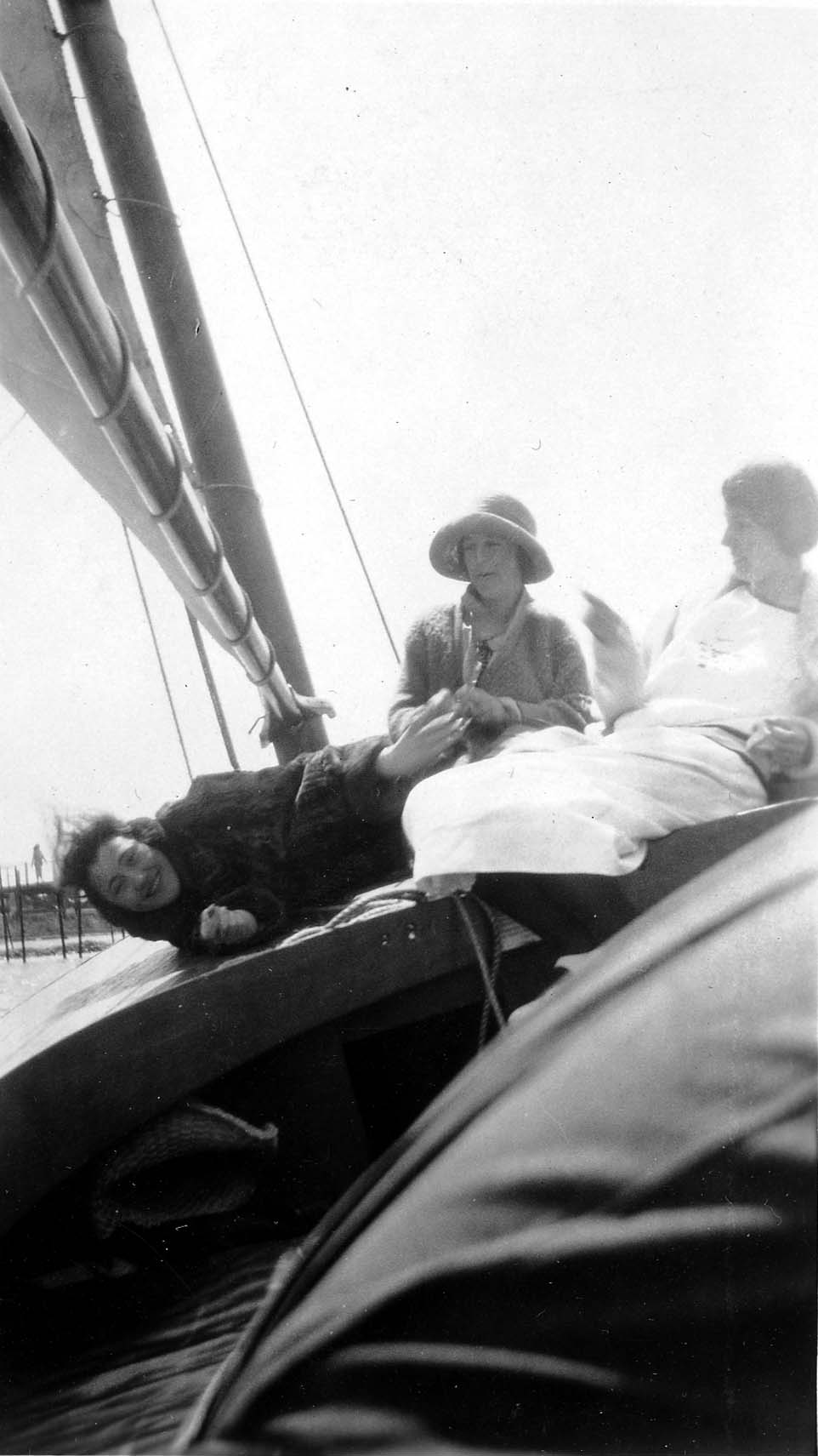 Three women relaxing on the deck of a sailboat, with the boom and rigging visible overhead.
