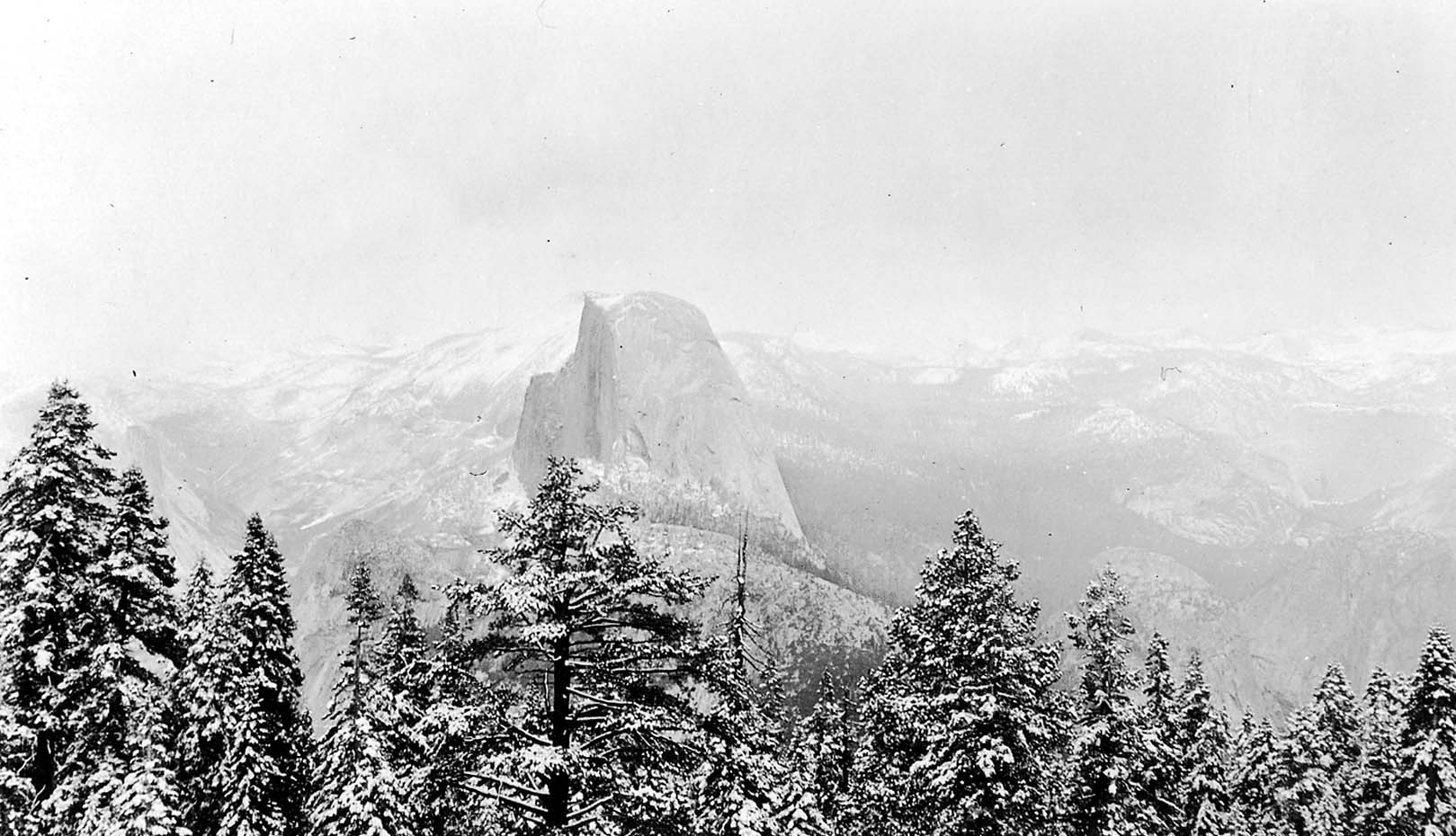 A sweeping panoramic winter view of Half Dome and the High Sierra peaks heavily blanketed in deep snow from Glacier Point.