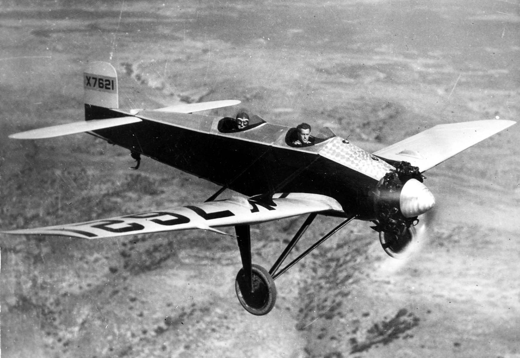 A low-angle air-to-air photograph of the Hall X-1 prototype X7621 banking in flight over rugged chaparral hills in San Diego County.
