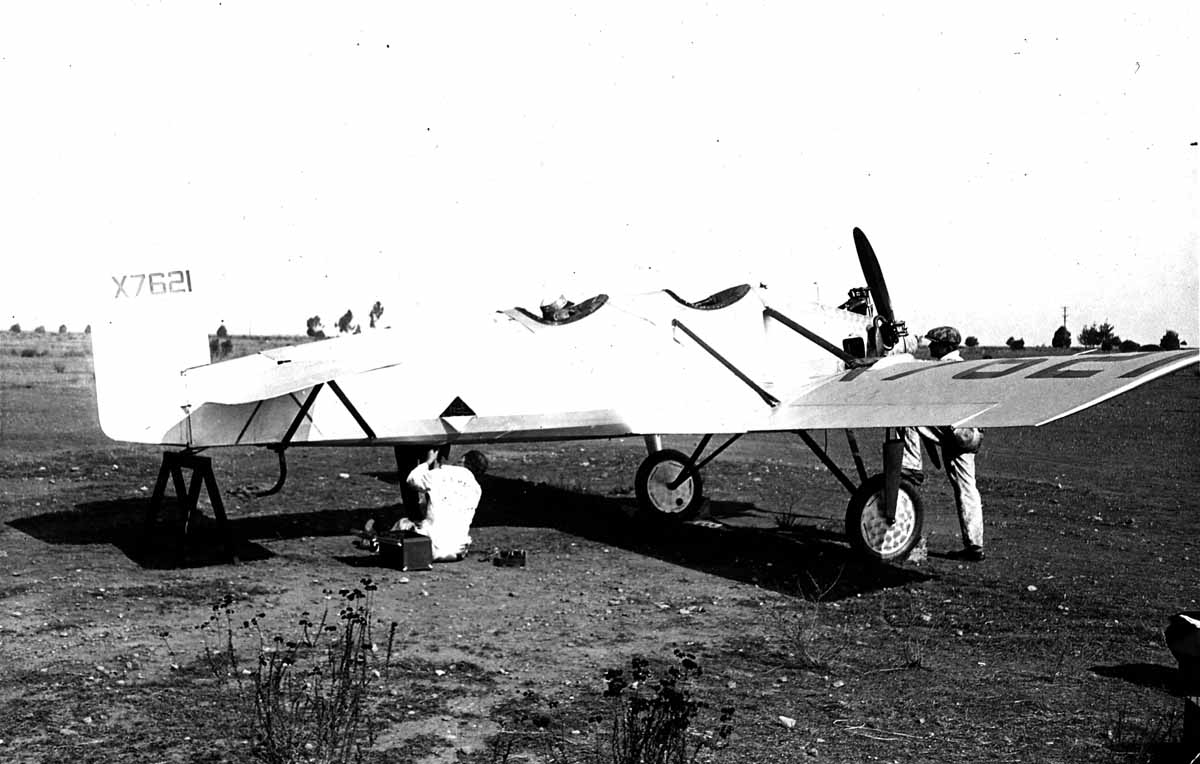 Ground crew mechanics in white overalls servicing the engine and undercarriage of the Hall X-1 elevated on a wooden maintenance horse.