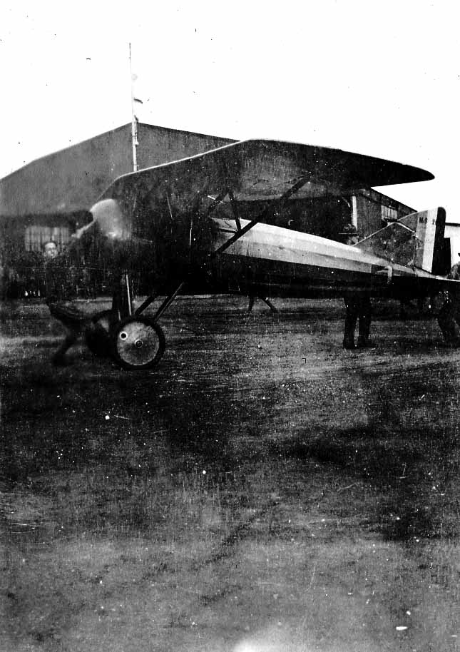 A mechanic swinging the wooden propeller to start a Morane-Saulnier MoS-30 parasol monoplane as an Army officer watches on an airfield.