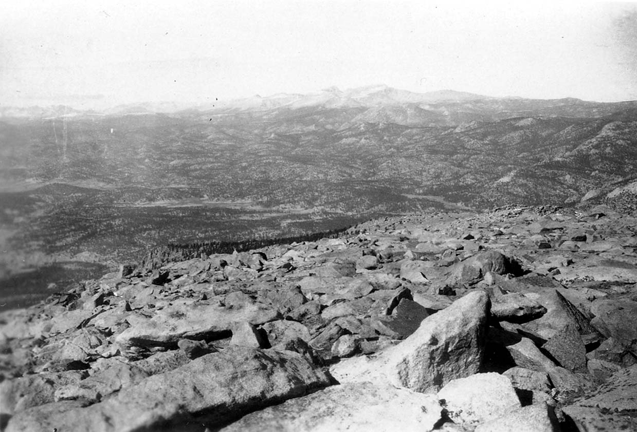 Uneven, rocky terrain sloping upwards toward a mountain crest in the distance well above the tree line.