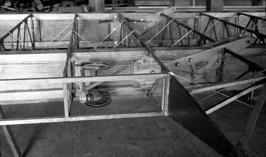 A detailed close-up of the exposed wooden wing ribs and the mechanical pulley and wire system used to control the aircraft's ailerons.