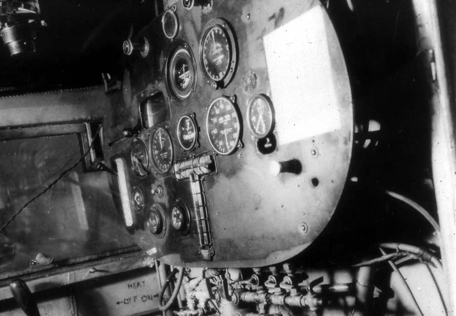 Interior photograph of the Spirit of St. Louis cockpit showing the instrument panel, periscope control, and fuel valve manifold.
