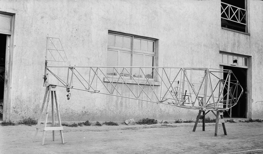 The raw, completed tubular steel fuselage framework of the Spirit of St. Louis resting on wooden sawhorses outside the Ryan Airlines factory building.