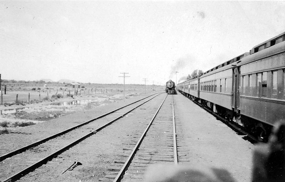 A steam locomotive approaching on railway tracks adjacent to a row of parked passenger train cars.