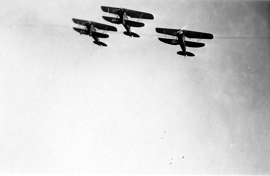 A clear, close-up air-to-air style view of three biplanes flying in a tight V-formation.