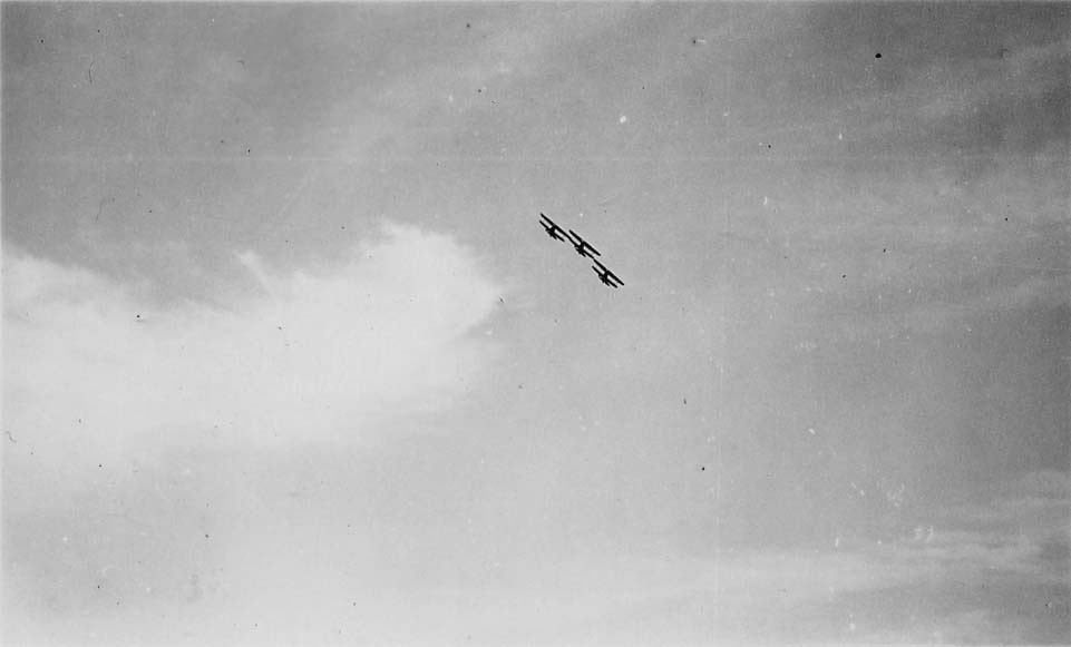A distant view of three biplanes executing a steep, coordinated climb against a cloudy sky.