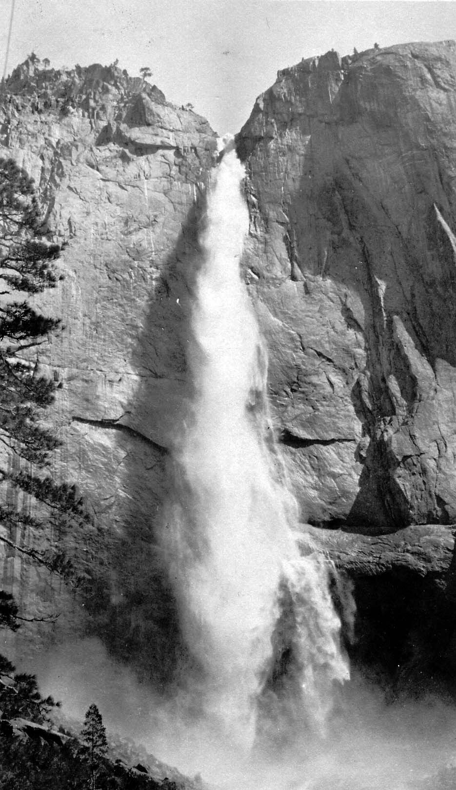 A towering vertical perspective of Upper Yosemite Fall plunging 1,430 feet down the sheer granite cliff wall into misty valley basins.
