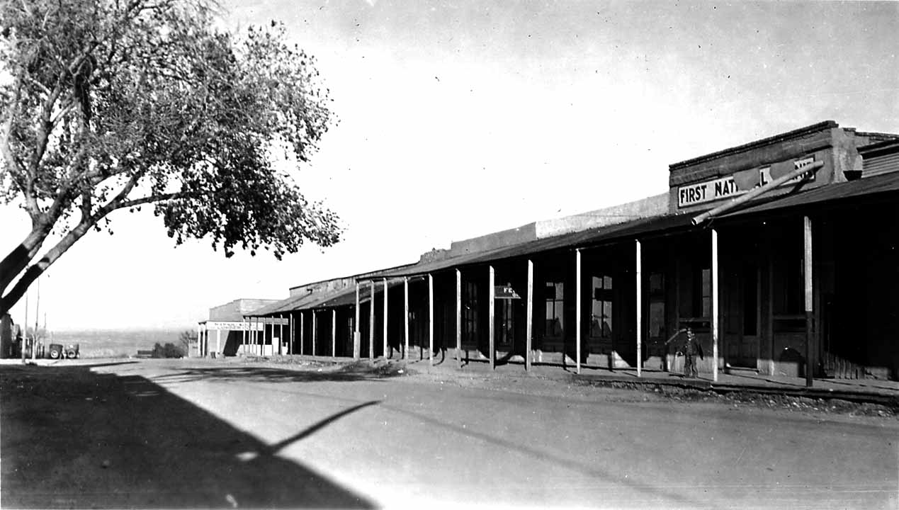 A view of a rustic western town street featuring a wooden boardwalk and a building clearly marked "FIRST NATL" bank.