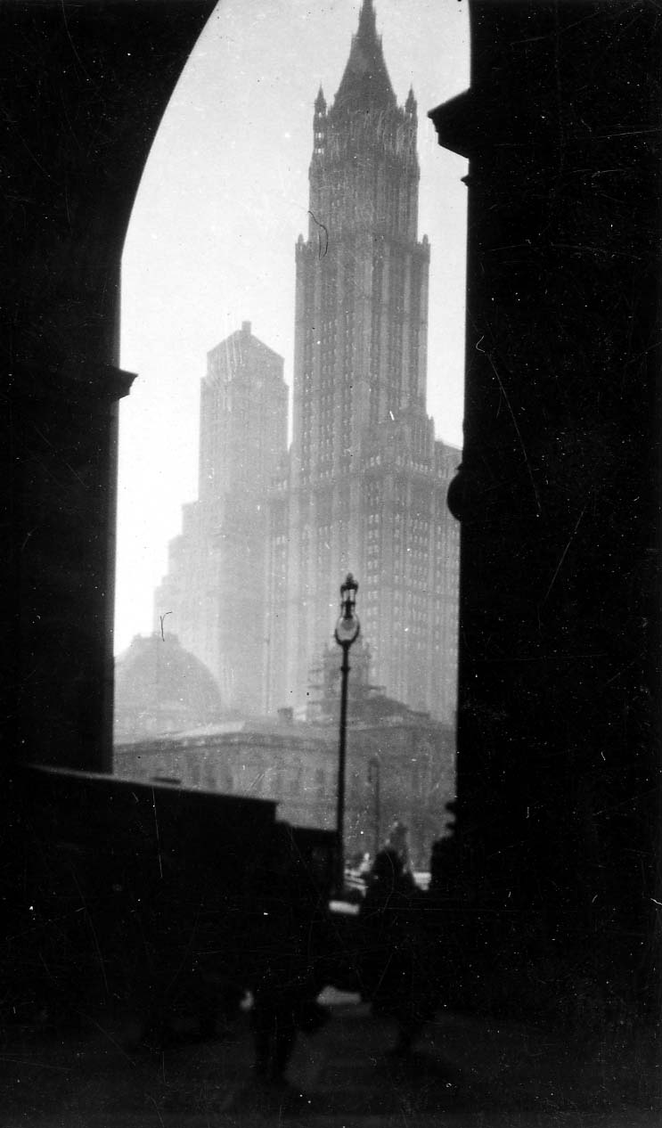 The iconic Gothic spire of the Woolworth Building framed dramatically through the grand classical arch of the Manhattan Municipal Building.