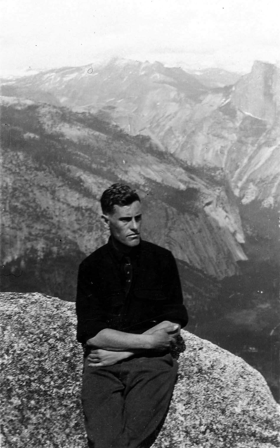 Donald A. Hall Sr. sitting on a high granite cliff overlooking a vast mountain valley.