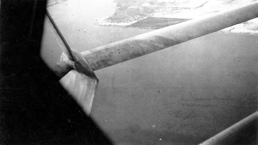 Aerial view from cockpit window looking along the streamlined wing strut down at the San Diego coastline and water.
