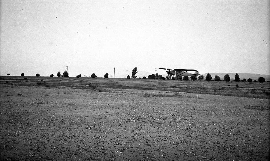 Long-distance airfield photograph of the Spirit of St. Louis airborne low over the Camp Kearny flight field.