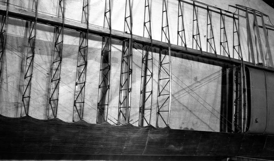 Overhead workshop view of uncovered 46-foot wooden wing framework showing spruce ribs, spars, and plywood leading edge.