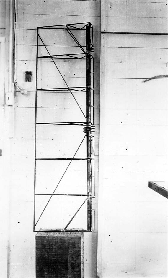 Vertical view of bare welded steel-tube aileron framework resting on wooden crate against workshop wall.