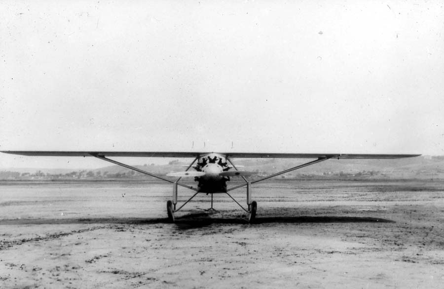 A vintage black and white photograph of an front view of the Spirit of St. Louis at Dutch Flats airfield in San Diego, California in May 1927. The photo shows the airplane during the center of gravity test with the tail section raised to simulate the typical flight position of the airplane. The plane was flown by pilot Charles Lindbergh to Paris, France. The image was taken by Donald A. Hall, who was the designer and Chief Engineer of the plane.