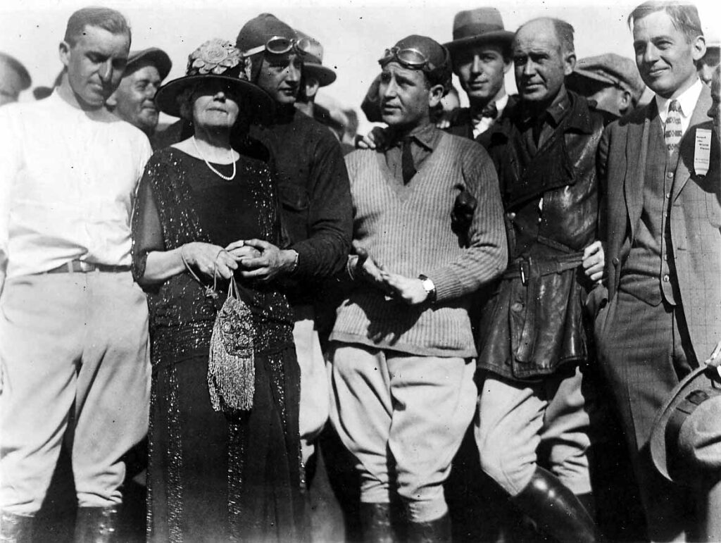 A vintage black and white photograph of Donald W. Douglas and a number of other aviators and men with the exception of one finely dressed older woman with pearls.