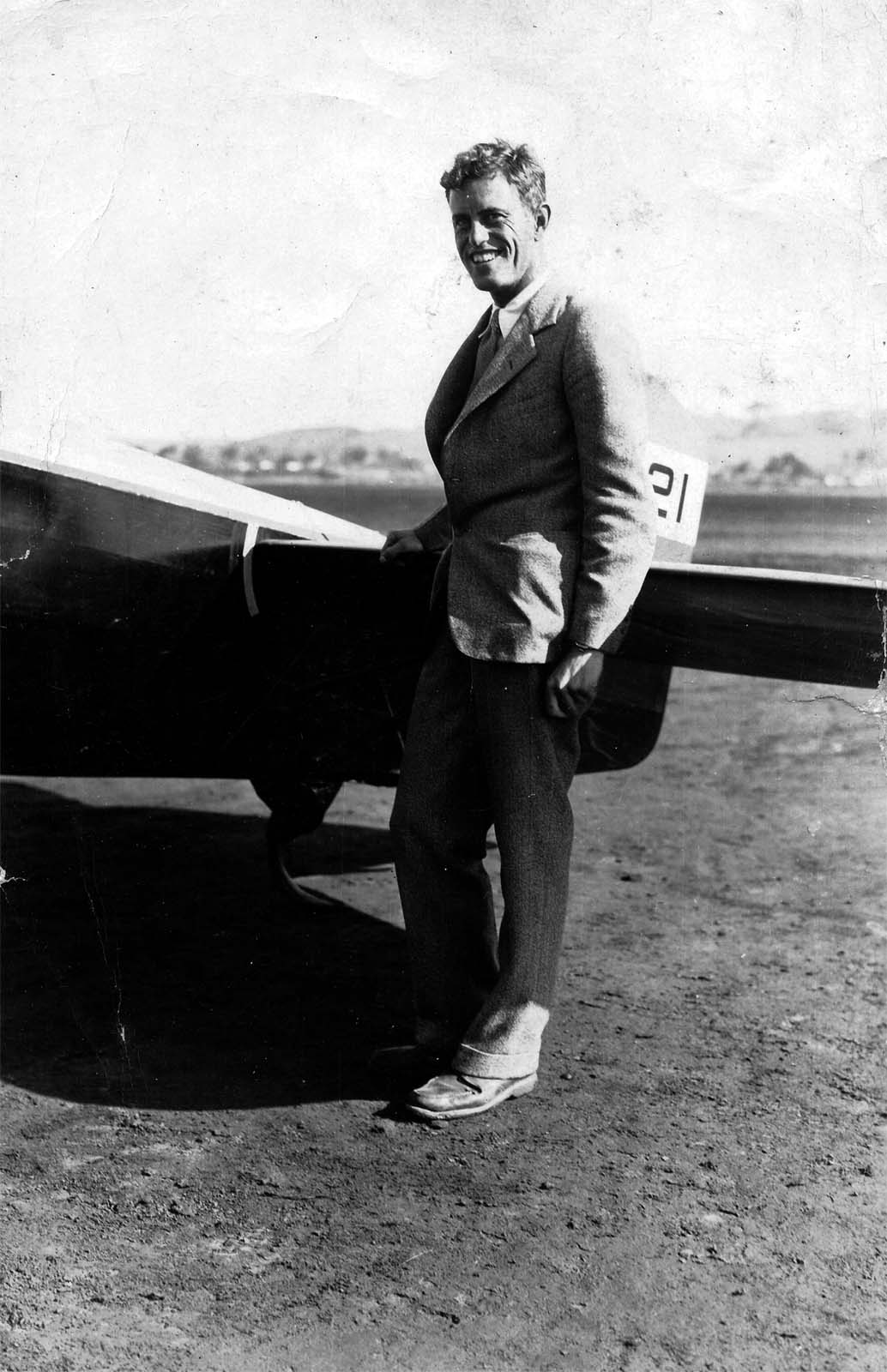 A vintage black and white photograph of engineer Donald A. Hall posing in front of the Hall X-1 testbed aircraft at Dutch Flats airfield in San Diego, California in 1929. Behind him is the patented all-moving horizontal stabilizer is called a stabilator.