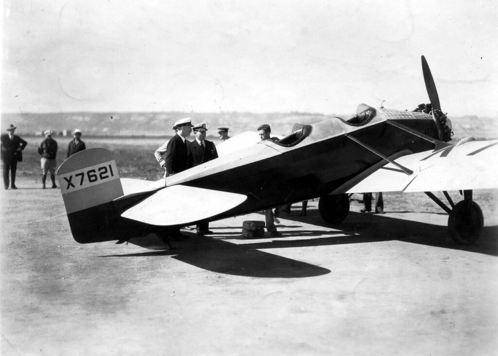 A vintage black and white photograph of Donald A. Hall standing behind the Hall X-1 testbed prototype aircraft as he formally meets with the Navy officers in 1929, at North Island in San Diego, California. The all-moving horizontal stabilizer is visable.