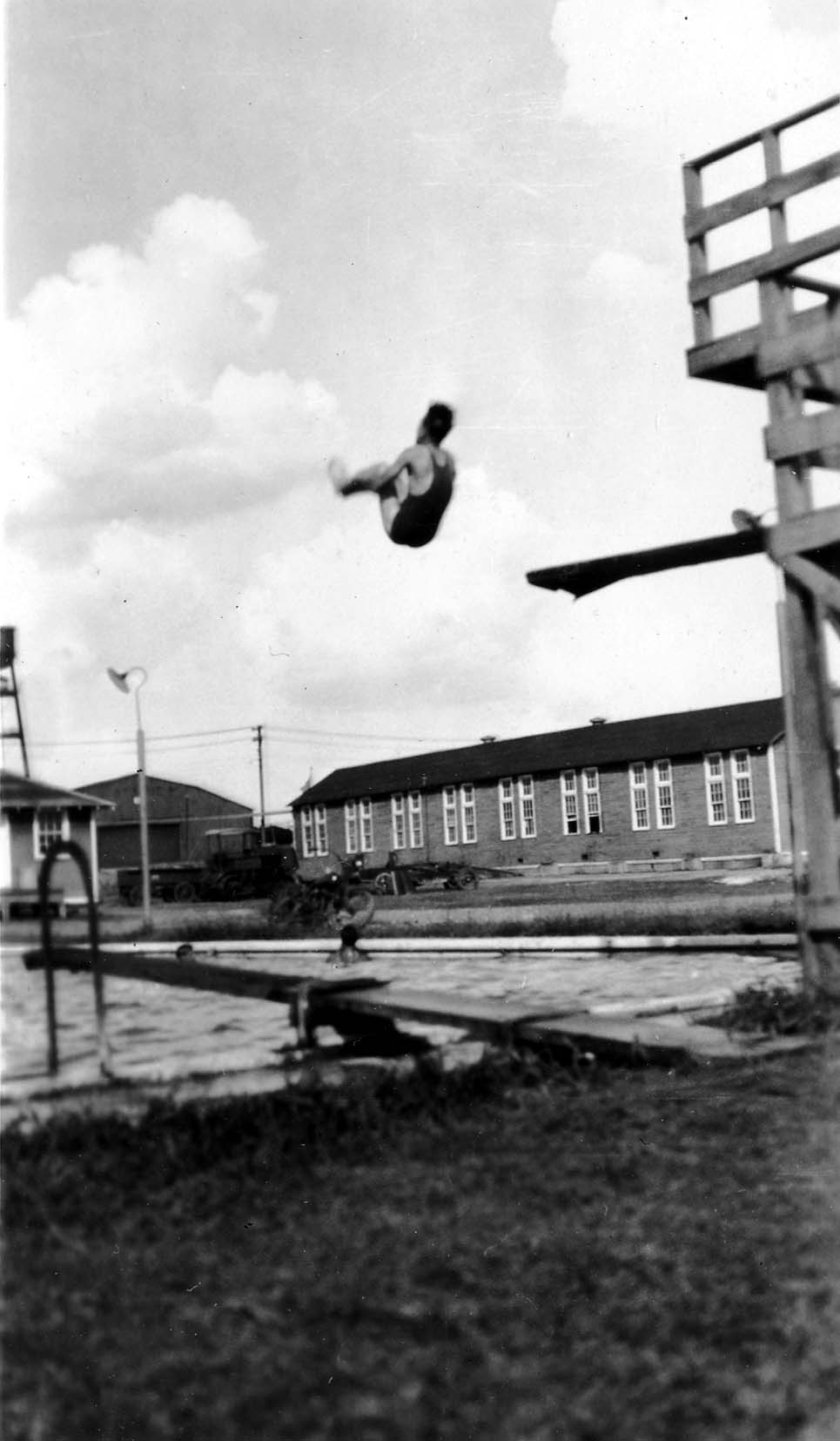 Vintage Black and White photograph of male diver captured in mid-air as he tumbles off a jumping board into a pool. Photo taken by Donald Hall in 1925 at Brooks Field Army base in Texas.