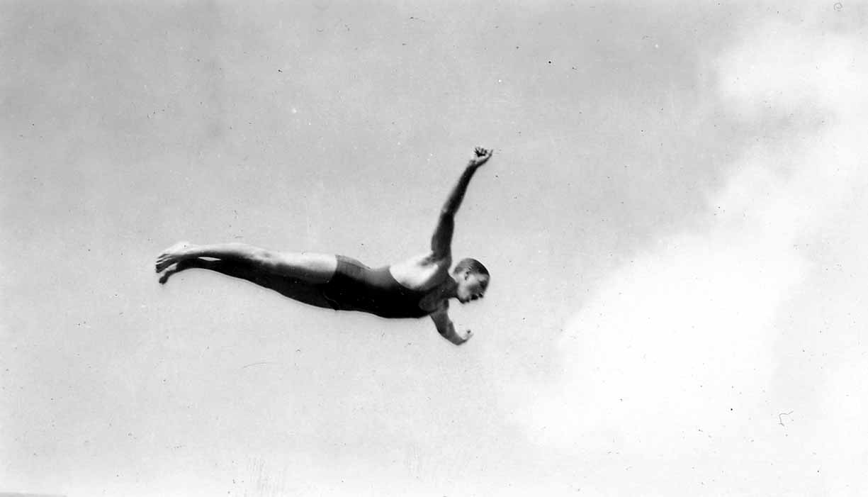 Vintage Black and White photograph of male diver captured in mid-air as he flies through the air. Photo taken by Donald Hall in 1925 at Brooks Field Army base in Texas.