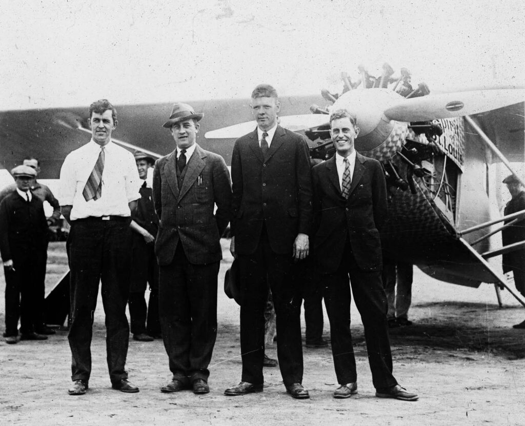 A vintage black and white team photograph of the Spirit of St. Louis with the owner Ben Mahoney of Ryan Airlines, production manager Hawley Bowlus, pilot Charles Lindbergh, and Chief Engineer Donald A. Hall. Hall has a huge smile. The image was taken in San Diego, California May 1927.
