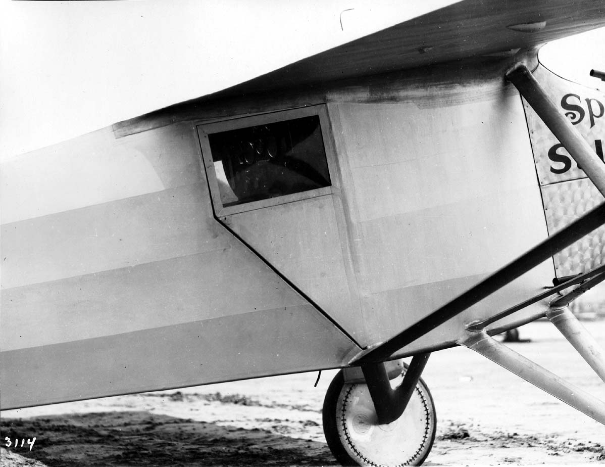 A vintage black and white photo of the Spirit of St. Louis's closed cockpit door, from the right side. Also visible is the trailing edge of the wing, struts, and the control panel. The photo was taken by Chief Engineer Donald A. Hall, in San Diego in May 1927.