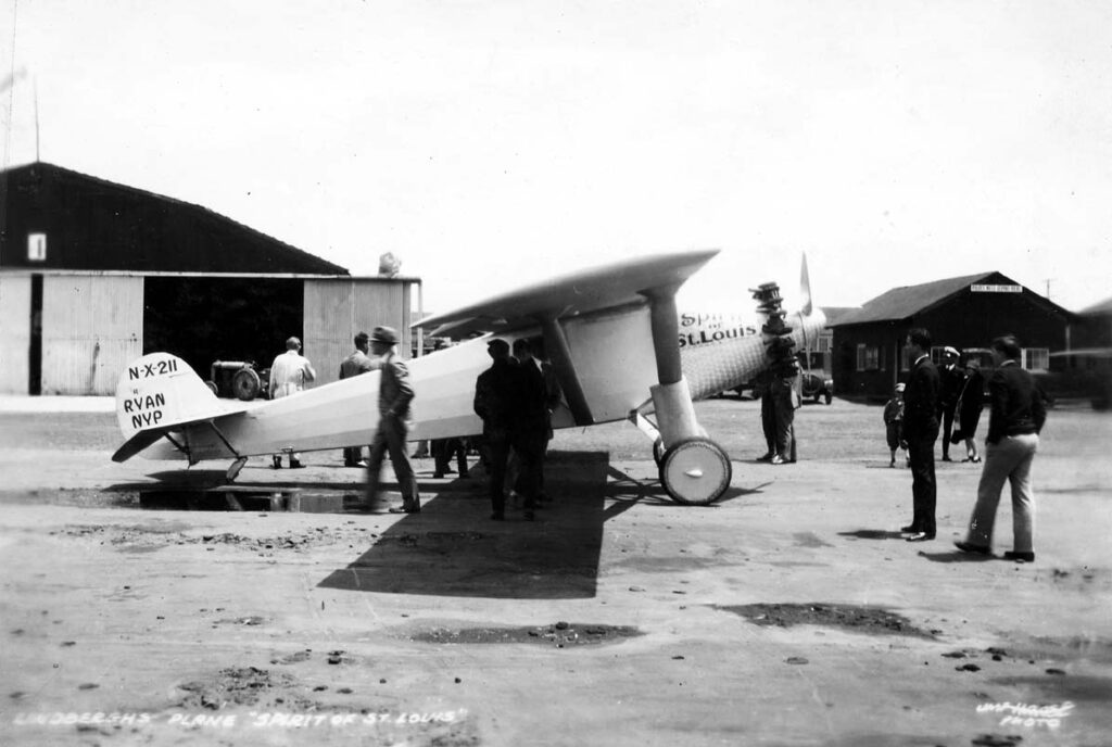 A vintage photo of the Spirit of St. Louis airplane from the side with the original nose cone. Probably taken in St. Louis on its way to Long Island, New York or in Long Island, 1927. Many men are looking at and inside the plane which pilot Charles Lindbergh successfully flew across the Atlantic non-stop.