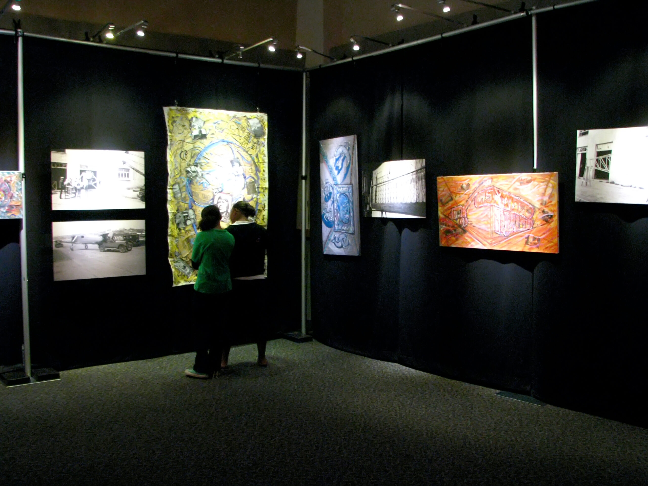 Image of two people viewing a painting by Nova Hall and his grandfather's photographs from the Flying Over Time Exhibition at Arizona State University in 2011 in Phoenix, Arizona.